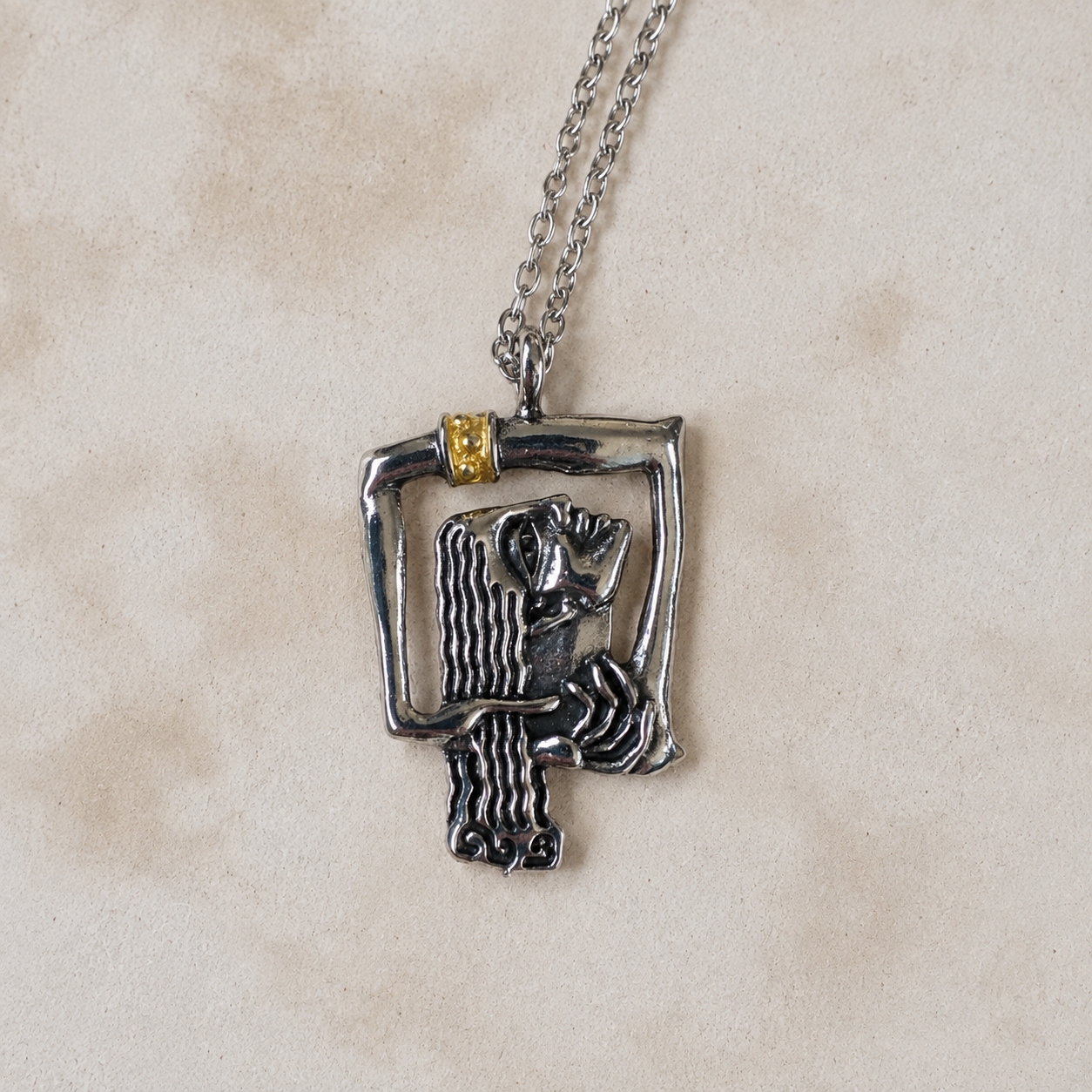 Close-up of a sculptural silver-tone female portrait pendant with dark detailing and gold-tone accent on a Bali inspired neutral tone stone wall 