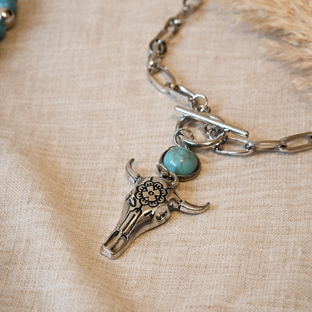 Close-up of a silver-tone bull skull pendant necklace with a turquoise-look bead detail festival wear matched on linen 