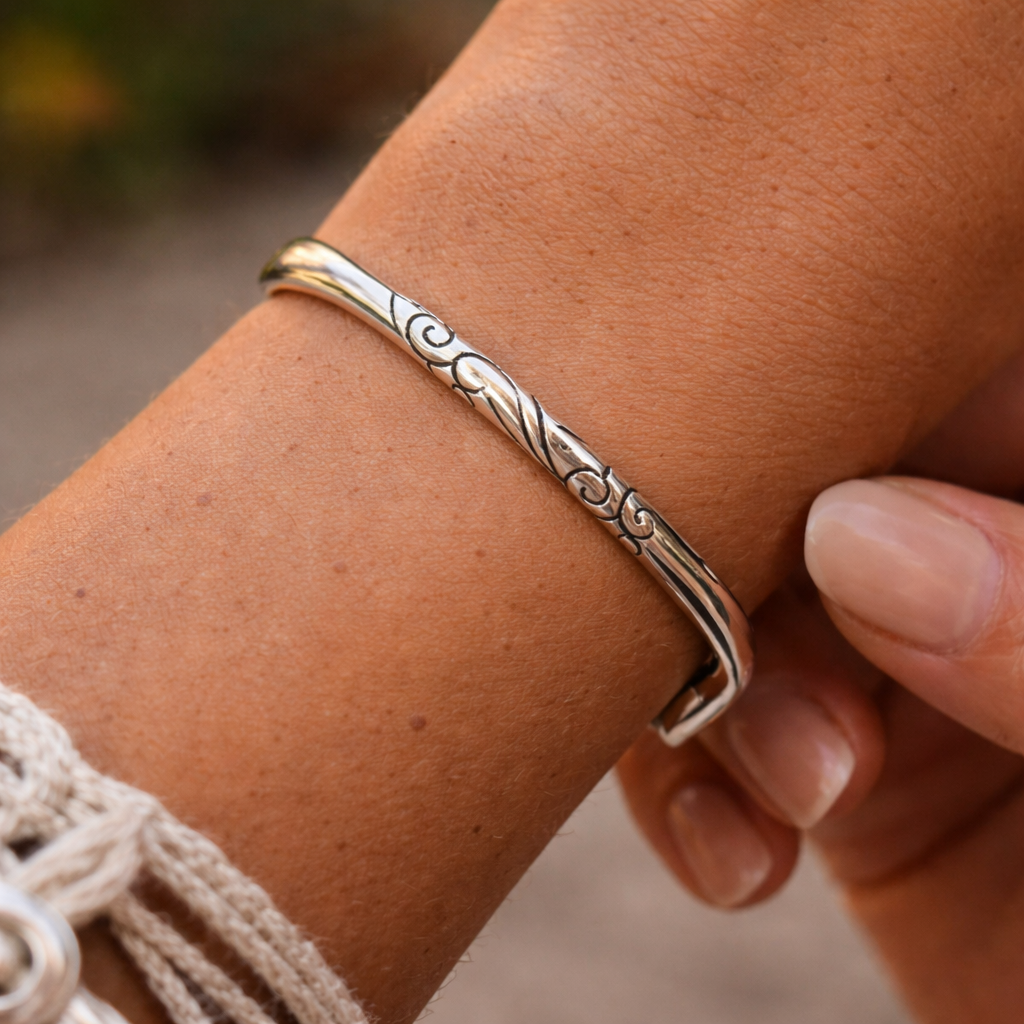 Side view of a silver-tone open cuff bracelet with engraved spiral pattern details
