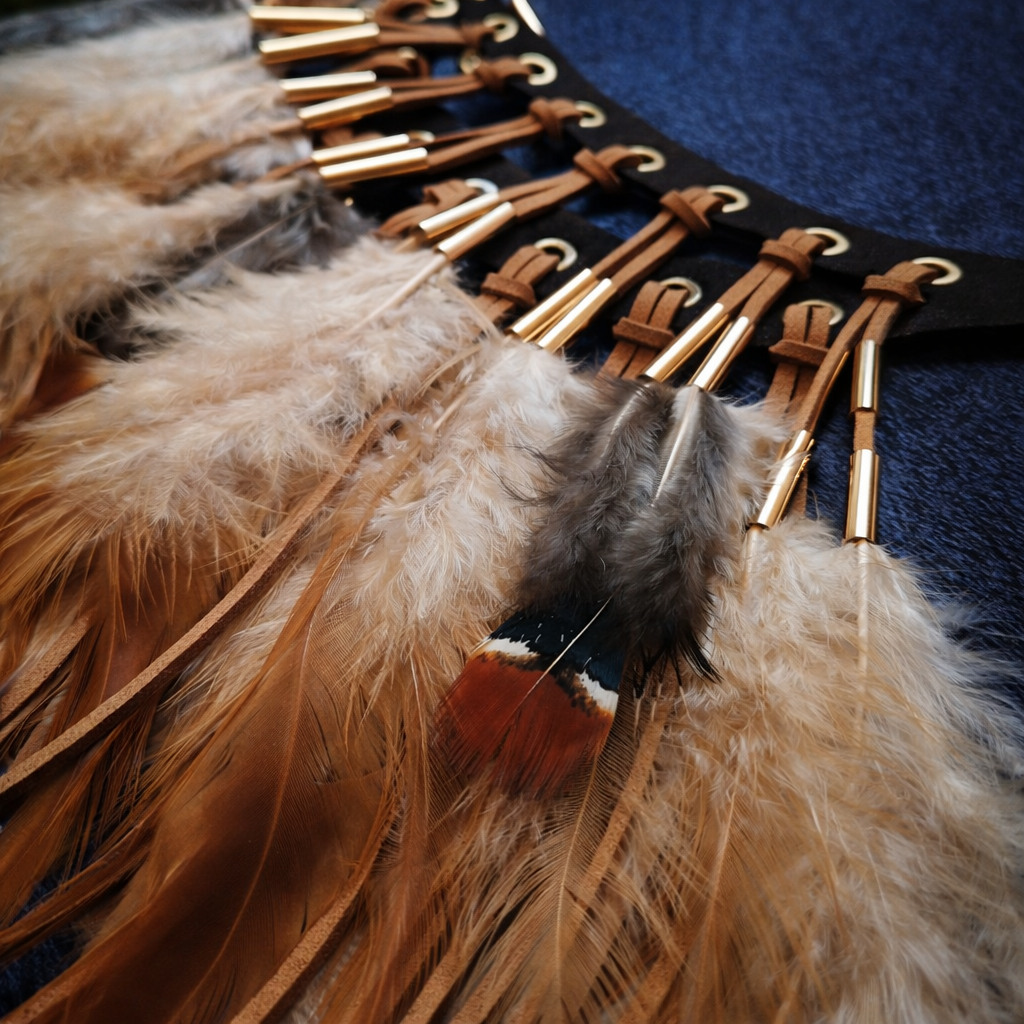 Close-up of a boho statement necklace with brown, cream, grey and black feather fringe, tan cords and gold-tone detail ready to wear for a festival 