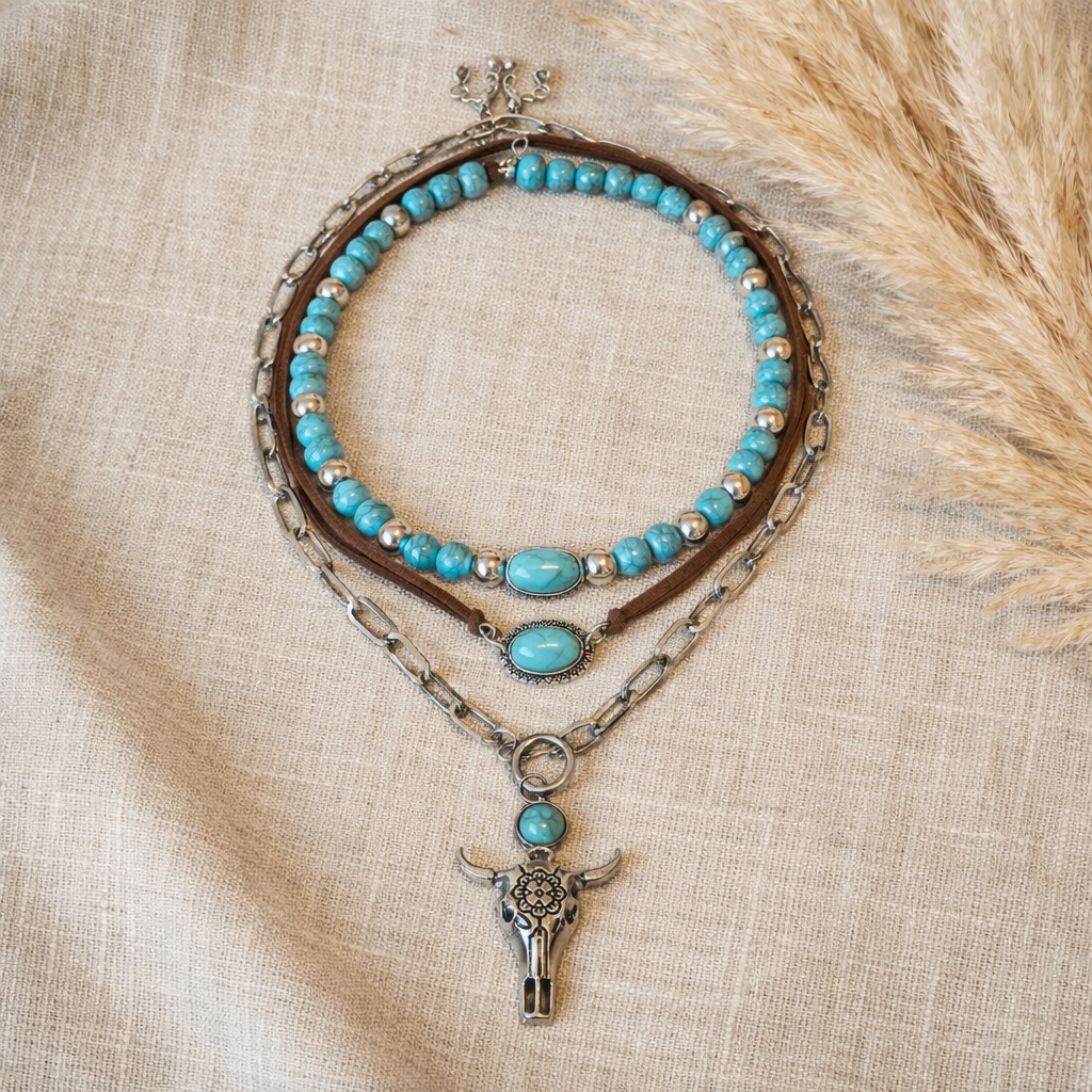 Boho festival wear necklace set with a bull skull pendant necklace, turquoise-look bead and brown leather necklace placed on linen