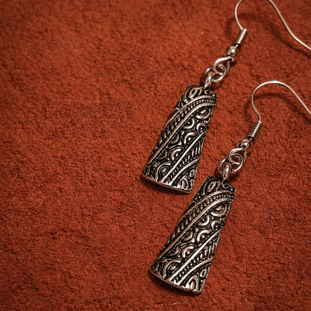 Pair of silver-tone geometric drop earrings with textured spiral-pattern details terracotta background