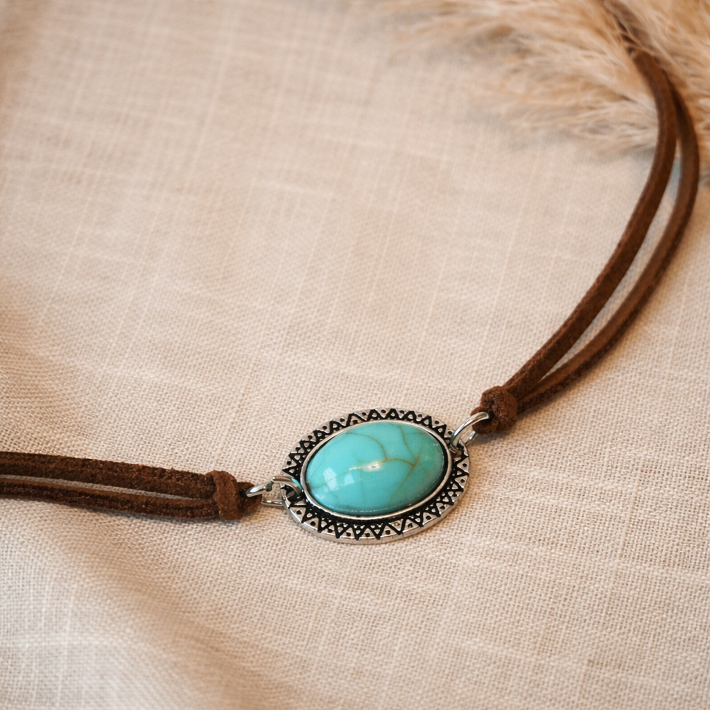 Brown leather necklace with an oval turquoise-look stone in a silver-tone decorative setting boho festival wear placed on linen 