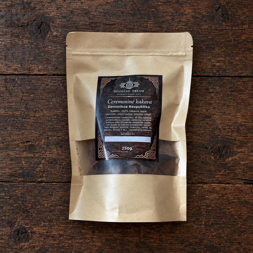 250 g pouch of Shamanic Dream ceremonial cacao from the Dominican Republic, shown on a dark aged wood surface.