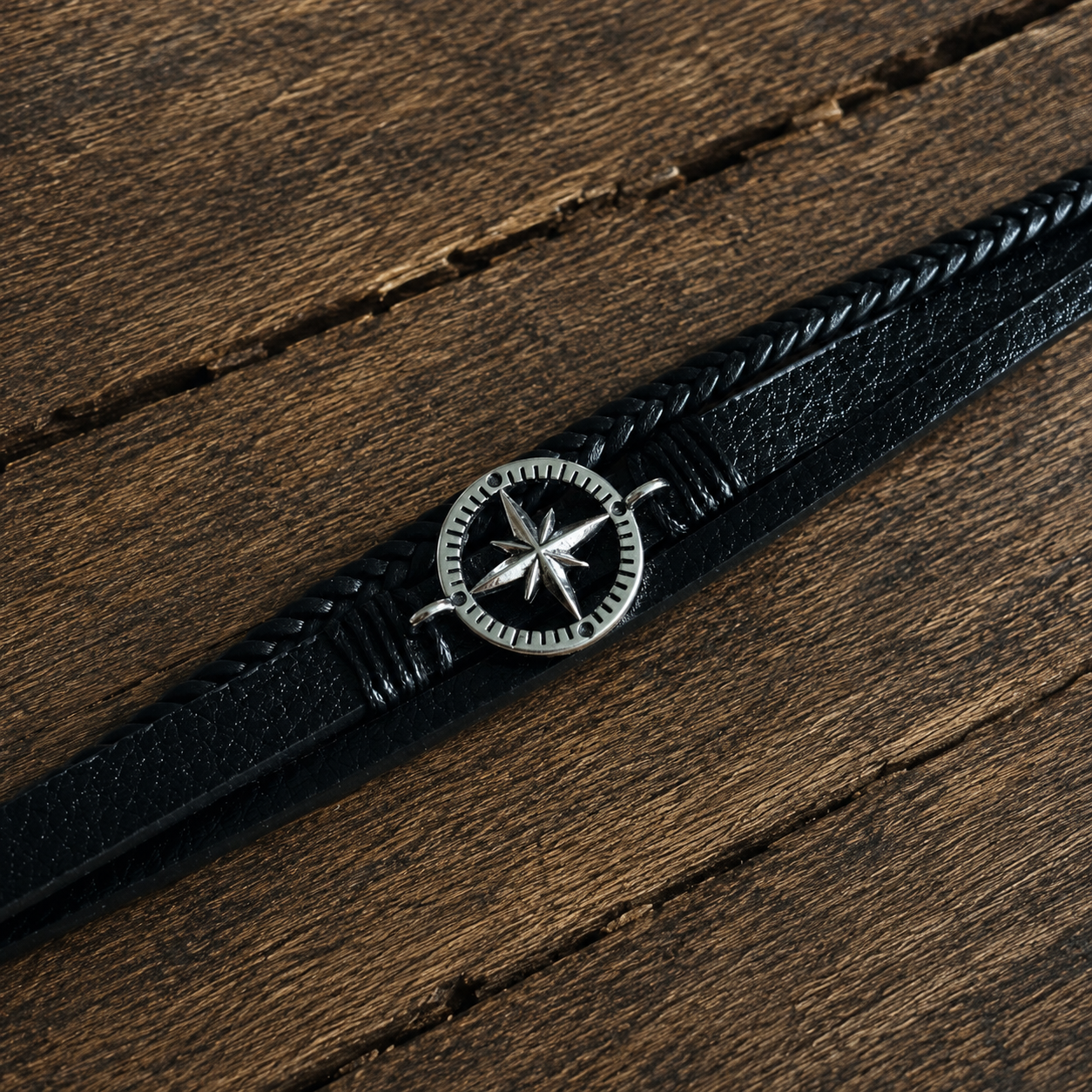 Black braided leather nordic style bracelet with a metal compass charm displayed on a rustic wooden surface.