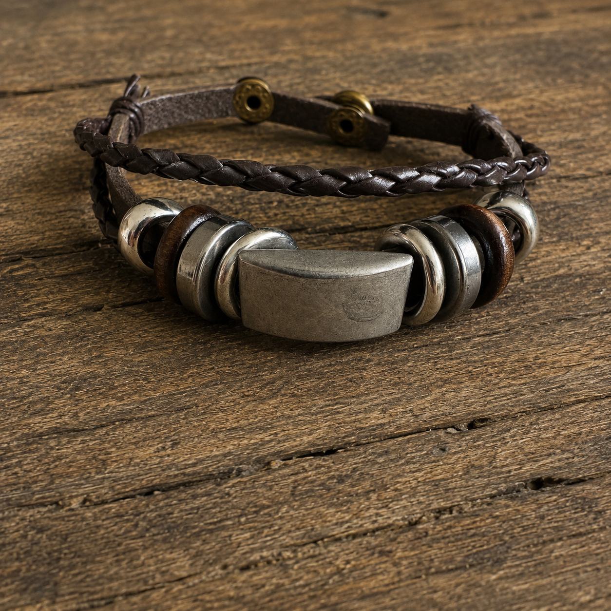 Handcrafted dark brown braided leather bracelet with metallic accents displayed on a wooden surface.