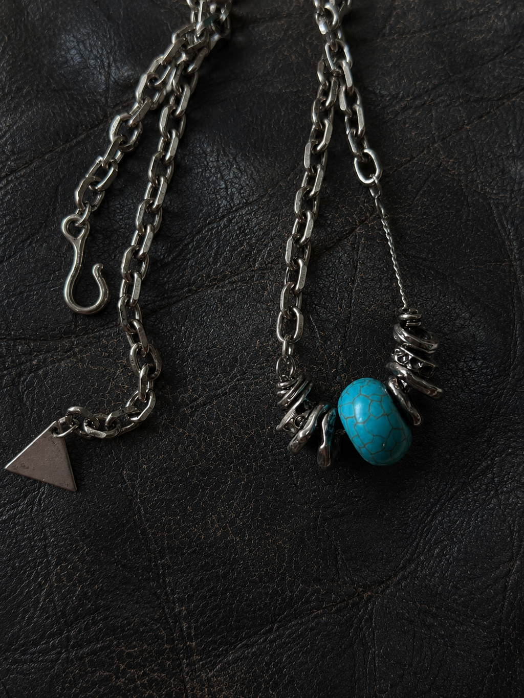 Close-up of a handmade blue stone pendant necklace with hand-wrapped metal accents on a black leather background