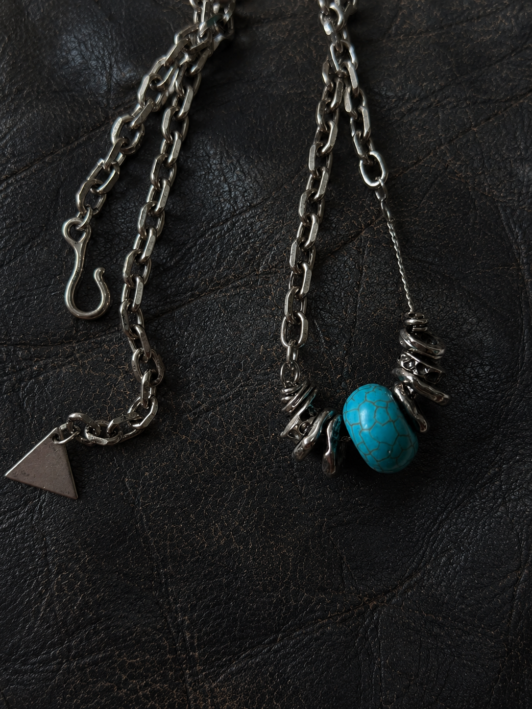 Close-up of a handmade blue stone pendant necklace with hand-wrapped metal accents on a black leather background
