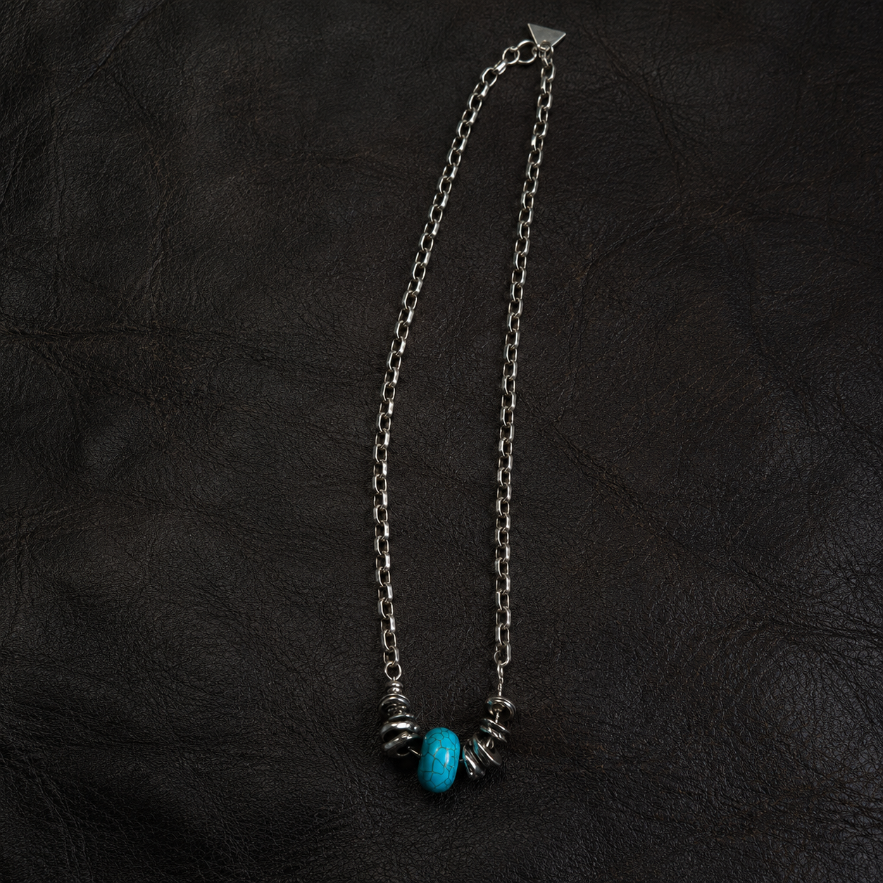 Handmade blue stone pendant necklace displayed on a black leather surface.