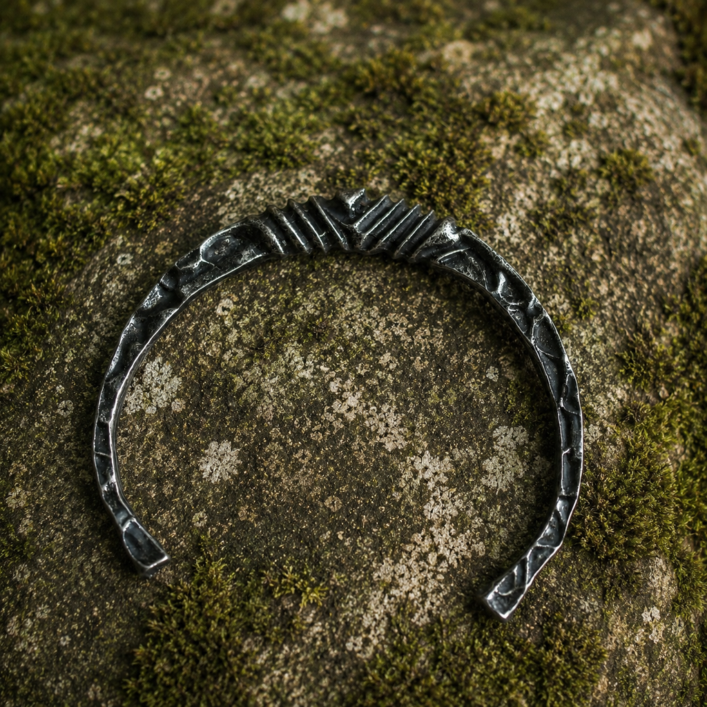 Forged Nordic open cuff bracelet with hammered texture displayed on natural stone.