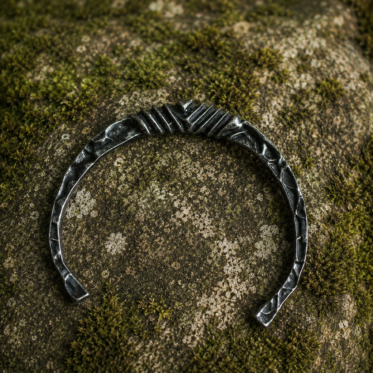 Forged Nordic open cuff bracelet with hammered texture displayed on natural stone.