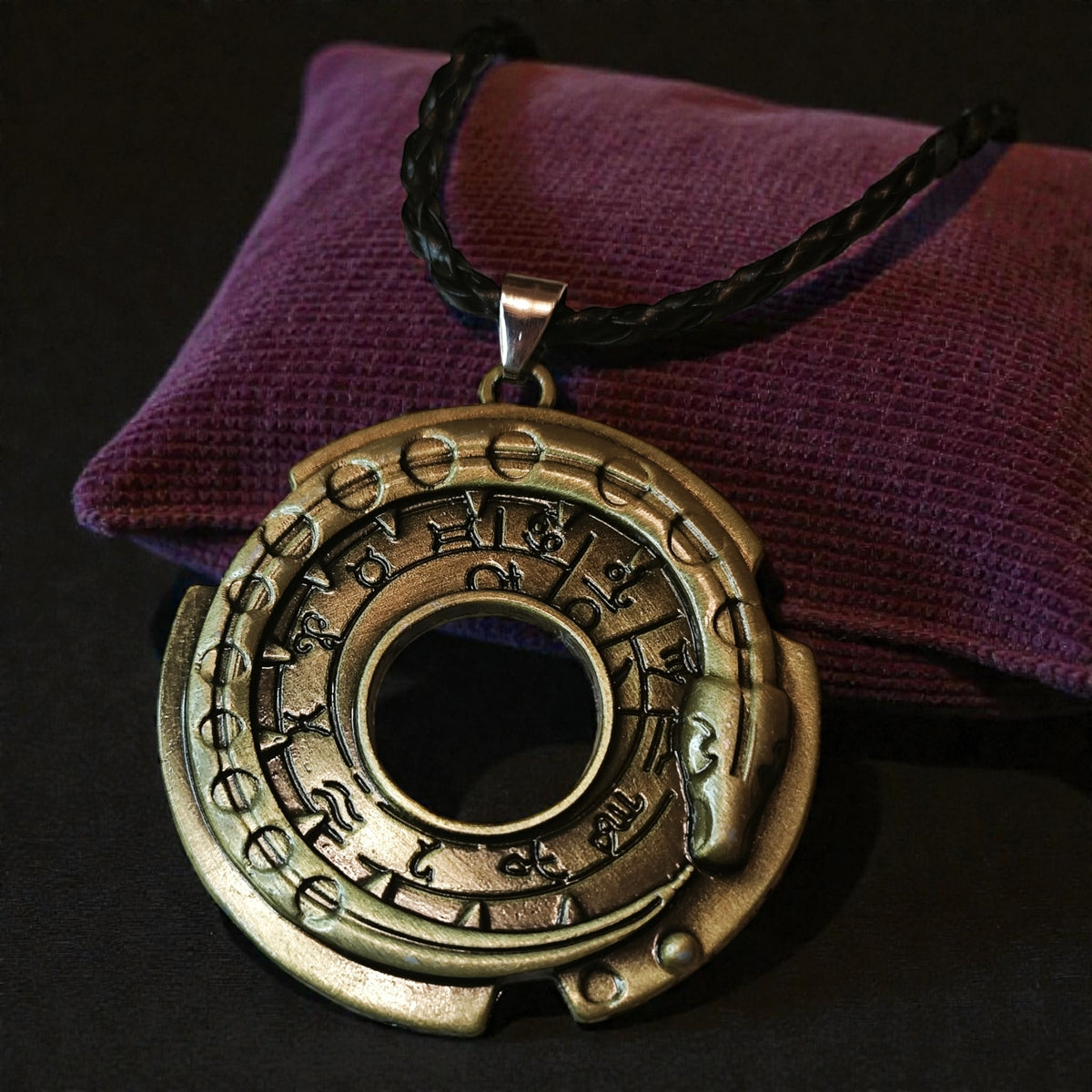 Close-up of a round gold-tone Norse-inspired rune snake wheel pendant on a black braided cord