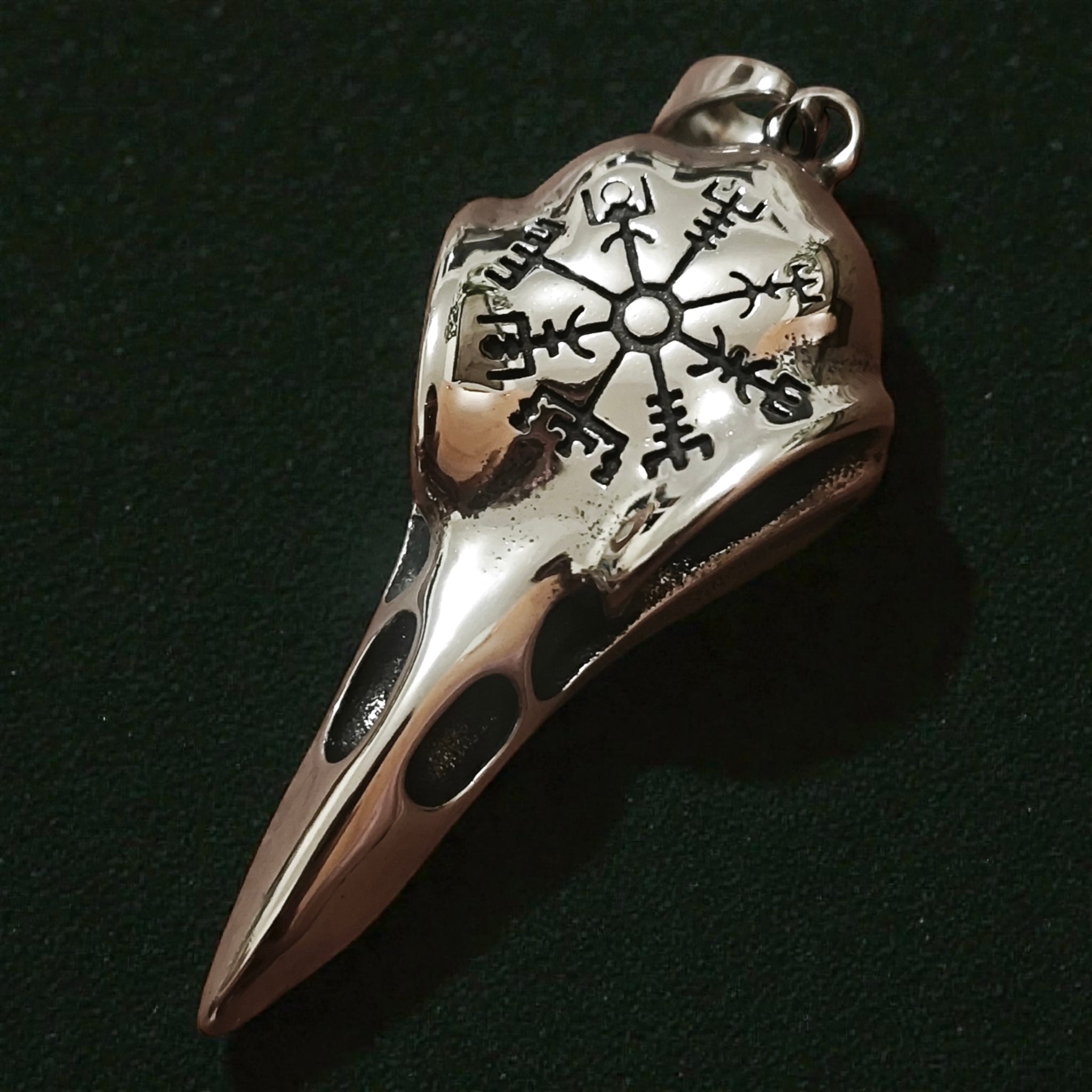 Close-up of a silver-tone raven skull pendant engraved with a Vegvisir-style symbol
