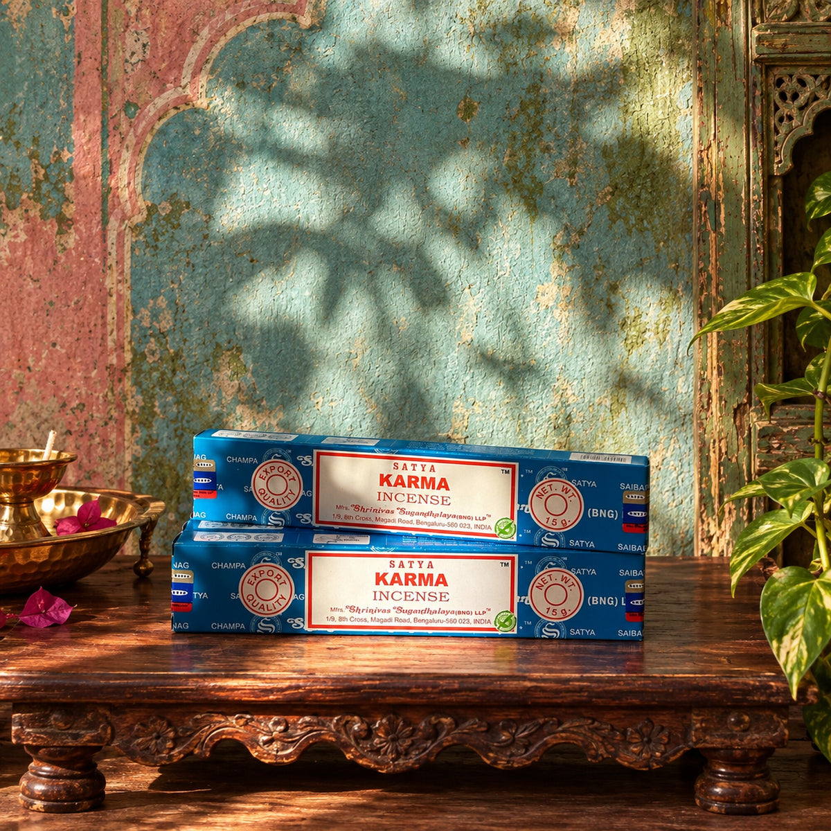 Two blue Satya Karma incense stick boxes, 15g, displayed on a carved wooden table against an Indian-inspired textured wall.