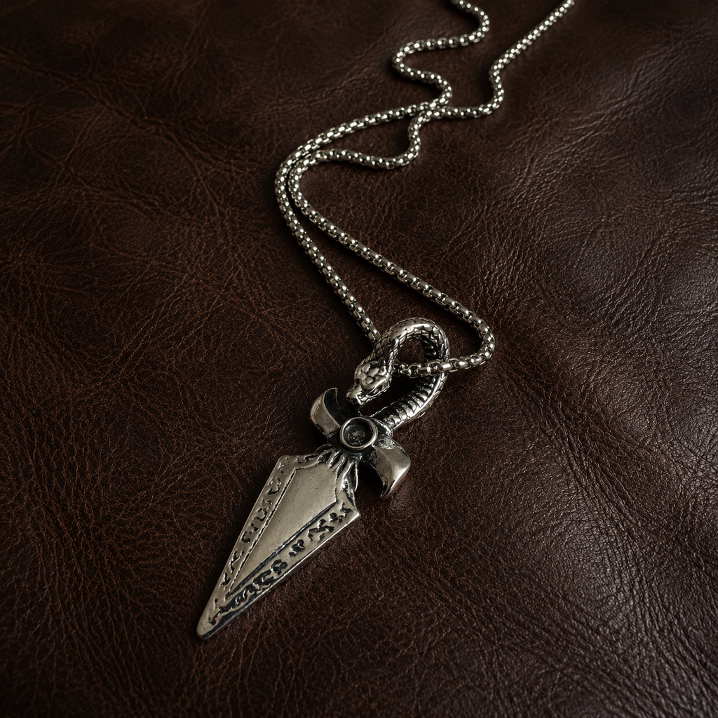 Stainless steel serpent and dagger pendant necklace with chain displayed on dark brown leather.