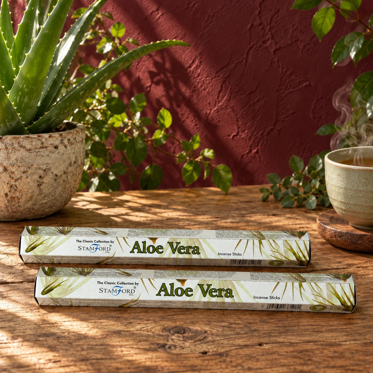 Stamford Aloe Vera incense sticks in white and green packaging on a wooden table beside an aloe plant and a ceramic cup.