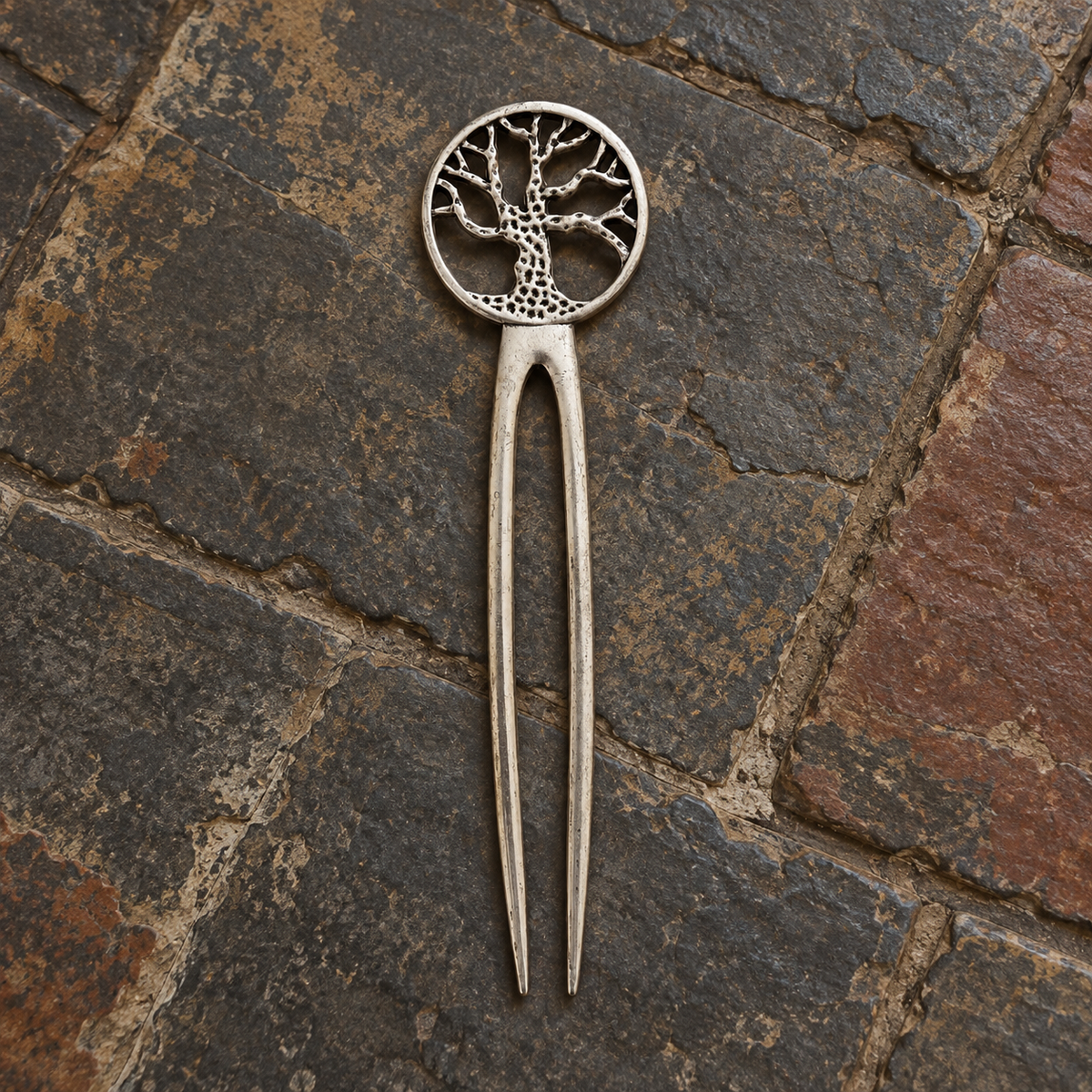 Full view of a 15 cm antique silver-tone Tree of Life two-prong hair pin on rustic stone flooring.