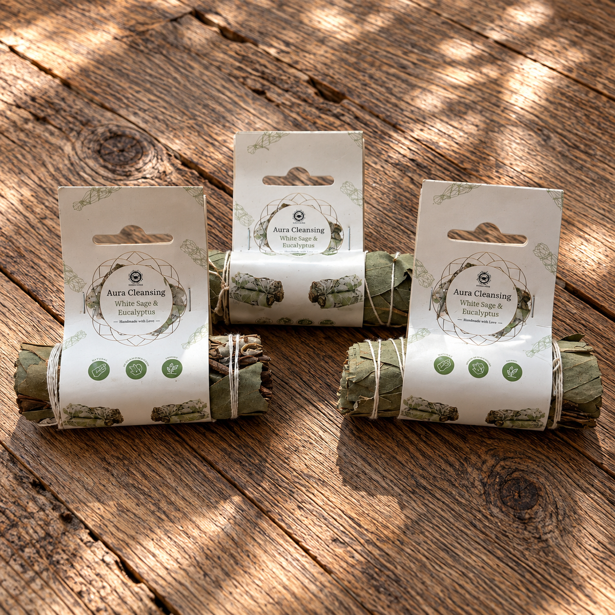 Three packaged white sage and eucalyptus botanical bundles, approximately 10 cm each, displayed on a rustic wooden surface.